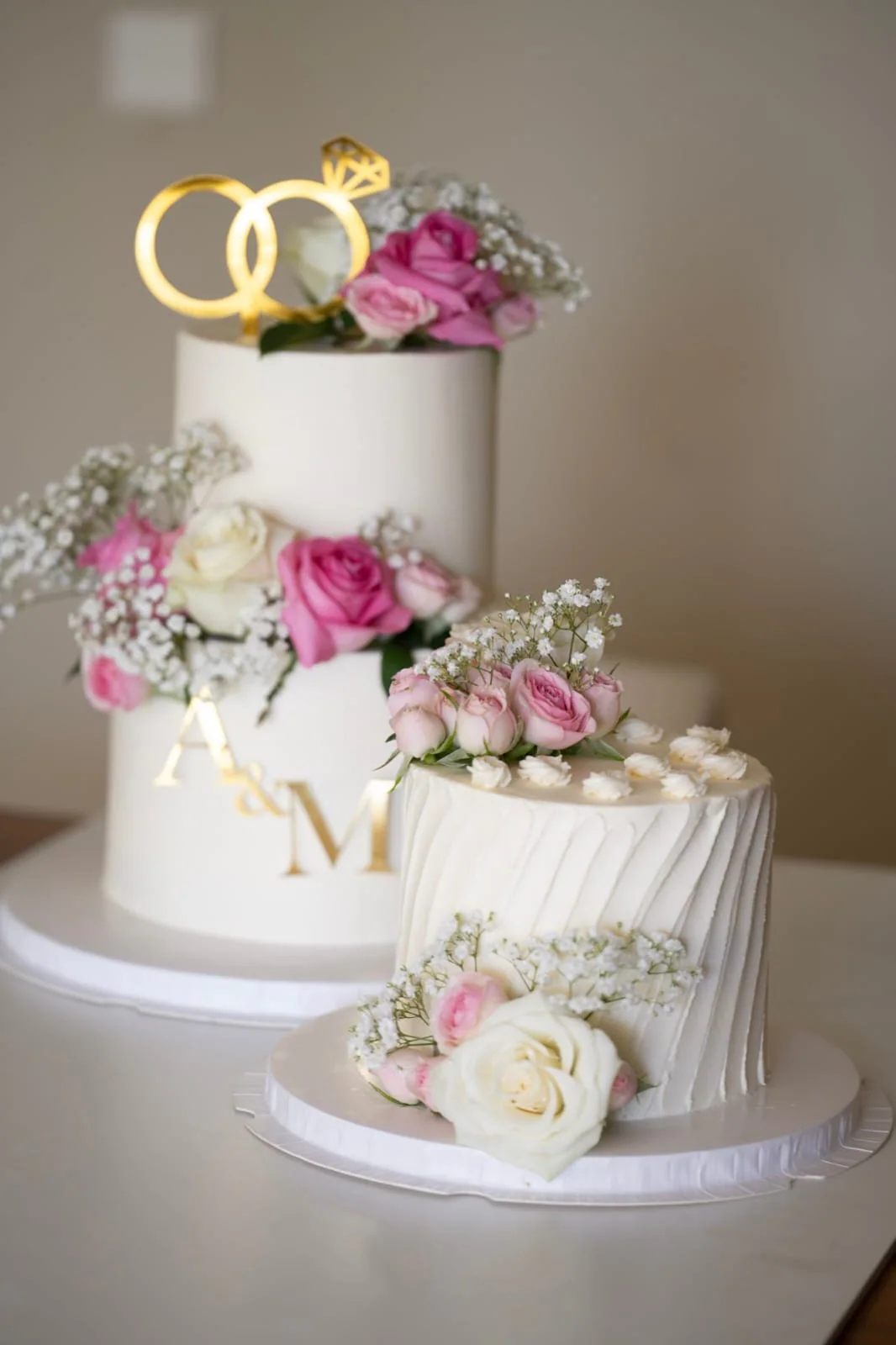 Two-tier engagement cake with gold rings and pink flowers