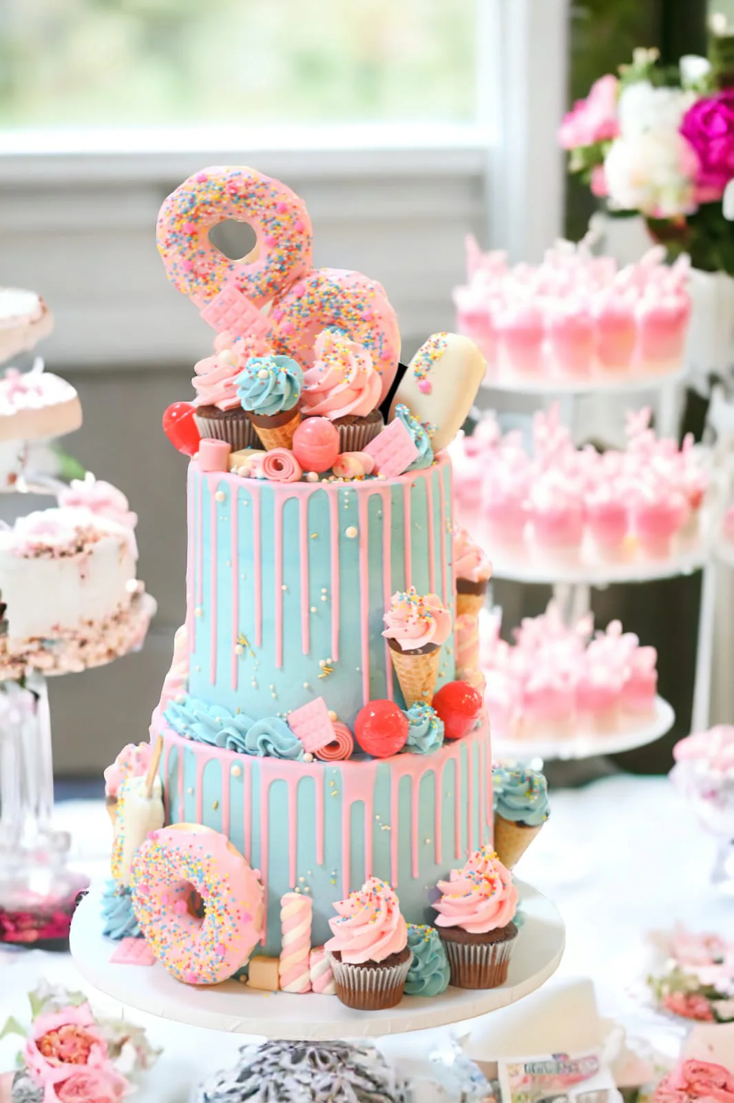Pastel two-tier dessert cake with donuts, macarons, and cupcakes